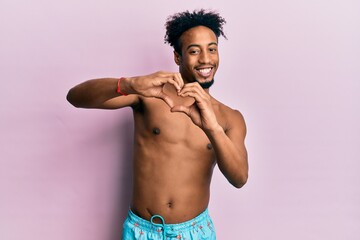 Fototapeta premium Young african american man with beard wearing swimsuit smiling in love doing heart symbol shape with hands. romantic concept.