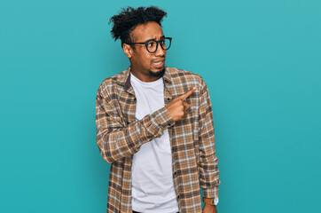 Young african american man with beard wearing casual clothes and glasses pointing aside worried and nervous with forefinger, concerned and surprised expression