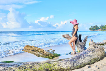 pregnant latina girl on the beach with black swimsuit and hat in summertime