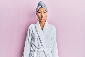 Young chinese woman wearing shower towel cap and bathrobe making fish face with lips, crazy and comical gesture. funny expression.