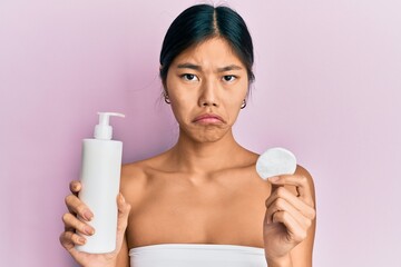Young chinese woman wearing shower towel using clean lotion depressed and worry for distress, crying angry and afraid. sad expression.