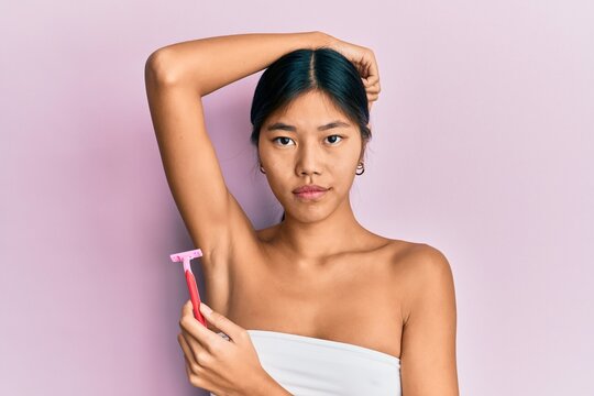 Young chinese woman wearing shower towel using razor skeptic and nervous, frowning upset because of problem. negative person.