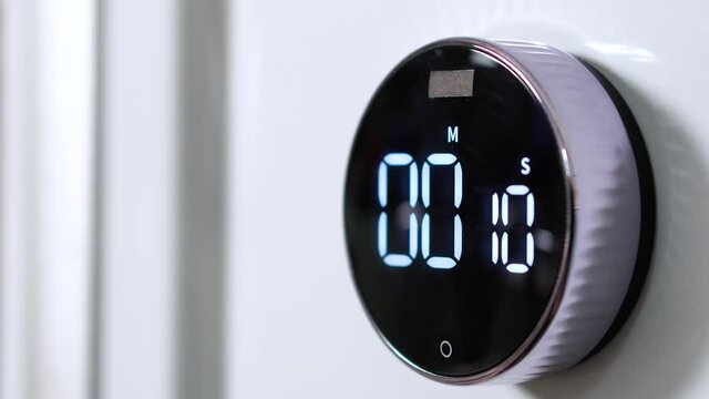 Closeup of gray round kitchen electronic and mechanical timer is set from 15 seconds to 0 and blinks