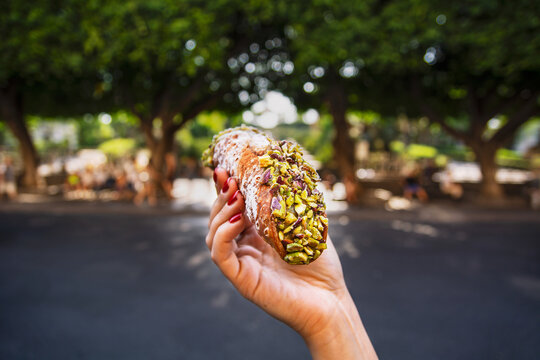 Female hand holding a pistachio cannoli in front of a park