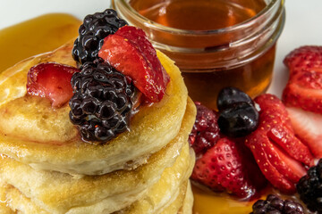 Tasty vegan, vegetarian butter dairy-free pancakes with berries topped, maple syrup on a white plate with black background. 