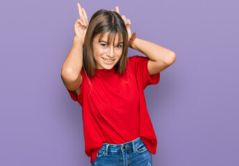 Teenager caucasian girl wearing casual red t shirt posing funny and crazy with fingers on head as bunny ears, smiling cheerful