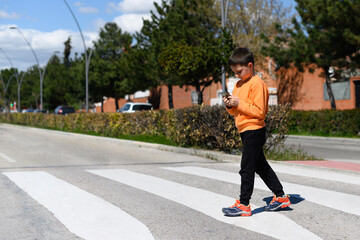 Child looks at a cell phone while crossing a crosswalk on a roadway