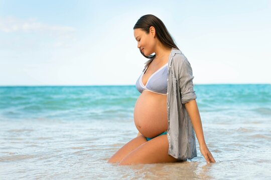 A beautiful pregnant woman relaxing in the water at the beach. Prenatal and motherhood.
