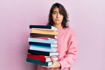 Young hispanic woman holding a pile of books depressed and worry for distress, crying angry and afraid. sad expression.