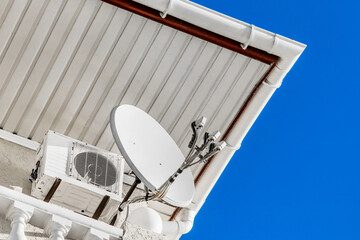 Satellite antenna transmitting signal next to the air conditioning under the roof of the hotel against the blue sky