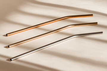 Sustainability concept. Eco friendly drinking straws from aluminium or stainless steel, reusable zero waste metal straw on neutral beige background with shadow from room windows, high angle view.