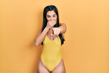 Young hispanic girl wearing swimsuit laughing at you, pointing finger to the camera with hand over...