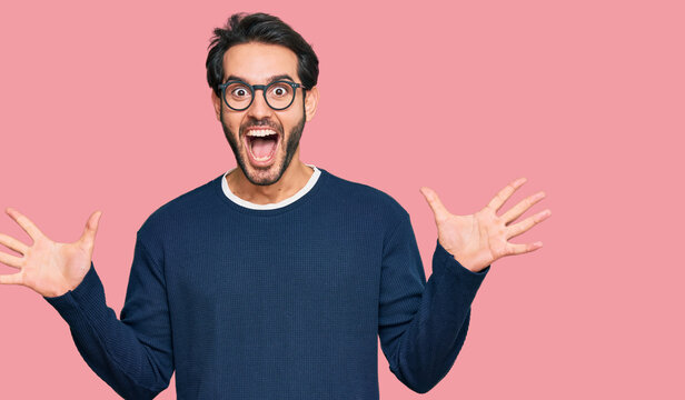 Young hispanic man wearing casual clothes and glasses celebrating crazy and amazed for success with arms raised and open eyes screaming excited. winner concept