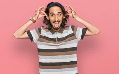 Young hispanic man wearing casual clothes smiling pulling ears with fingers, funny gesture....