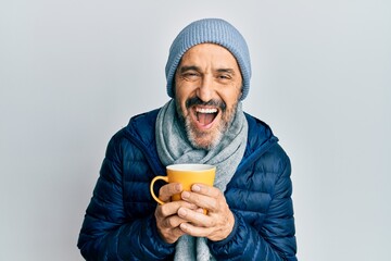 Middle age hispanic man wearing winter scarf and drinking a cup of hot coffee smiling and laughing...