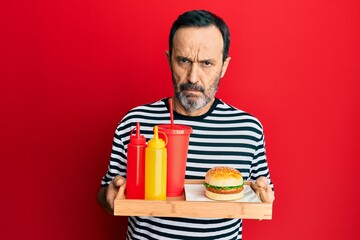 Middle age hispanic man eating a tasty classic burger and soda skeptic and nervous, frowning upset because of problem. negative person.
