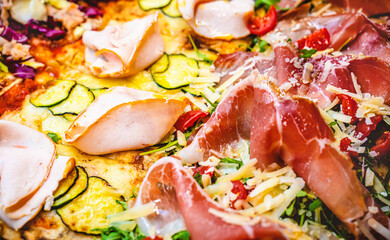 Fototapeta na wymiar Close up of different gourmet pizza slices with multiple colorful ingredients. Cherry tomatoes, zucchini, meat, ham, cheese