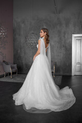 Fototapeta premium Full length bride portrait. Elegant female model wearing white fluffy wedding dress, standing and posing in grey room.