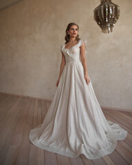 Fototapeta premium Full length bride portrait. Elegant woman in white wedding dress spinning in beige interior. Dynamic shot. Elegant female model standing and posing in ball gown