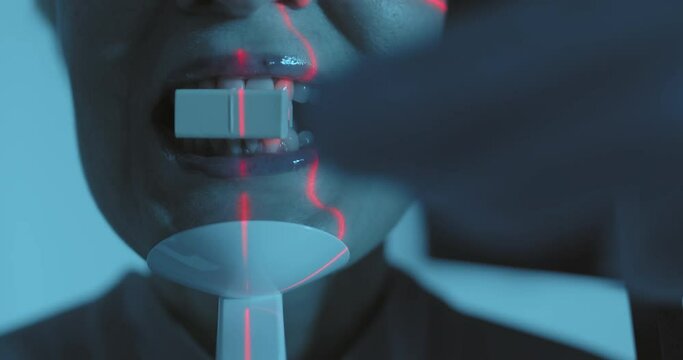 Close-up face of female patient with open mouth is standing in the 3D dental cone beam computerized tomography while a medical worker putting into the female patient mouth plastic detail.