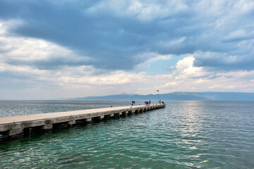 Fototapeta premium Turkey bursa 04.03.2021. Many people fishing on pier and port extends to marmara sea during overcast weather and rainy day. Sunshine coming after clouds.