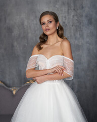 Elegant beutiful bride in white dress standing and posing against grey wall.