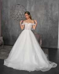 Young beautiful female model wearing long white bridal wedding dress standing and posing in grey...