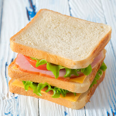 Tasty sandwich with ham, salad, cheese and tomatoes on rustic wooden table, close-up view, vertical orientation