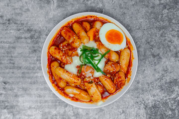 Top view Tteokbokki (Spicy Rice Cakes) with boiled eggs and cheese on the grey concrete table, Korean street food.
