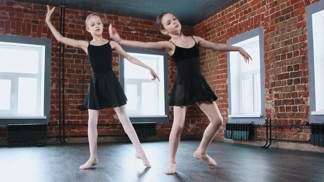 Ballet dancing indoors - two little gymnastics girls synchronously dancing in black dresses on training