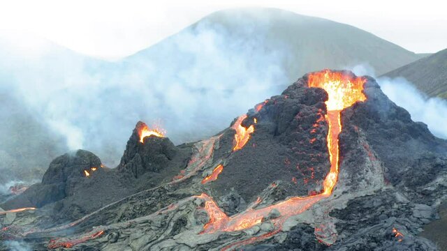 Aerial view of eruption of volcano and people watching flowing lava and crater. Fagradals mountain, Iceland, tilt up drone shot
