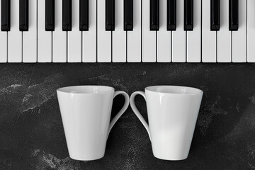 Keyboard of a piano with two white mugs in front of it on black background