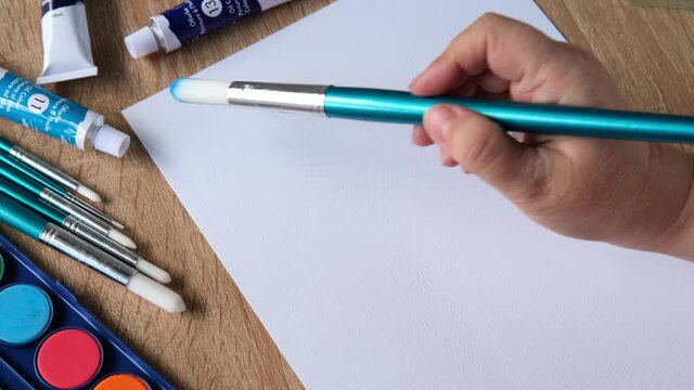 female artist's hand draws with colored paints, blue sky with clouds, background, abstract spots spread on white textured paper, watercolor painting, concept of creative art, art therapy