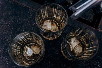 Top view of three glasses with alcohol and ice cubes standing on the table.