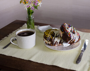 Cup of tea and glazed donuts  with chocolate and colorful sprinkles on a wooden table.