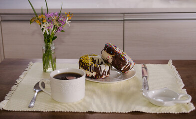 Cup of tea and glazed donuts  with chocolate and colorful sprinkles on a wooden table.