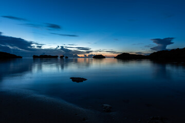 Introspective blue scene of Hoshizuna beach after sunset with orange horizon, sea and blue sky. Some stones in the backlight. Long exposure. Iriomote Island.