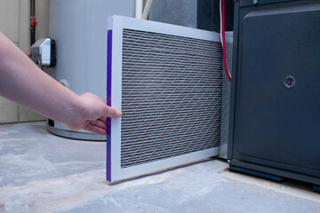 A person changing a dirty used air filter on a high efficiency furnace