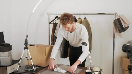 Cute curly young man packs clothes in a cardboard box to send