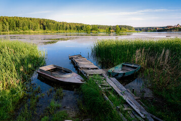 Old boats near a wooden pier in the reeds on the lake near the village in the morning