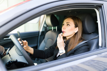 Fototapeta na wymiar Side view of a beautiful businesswoman putting lipstick in the car