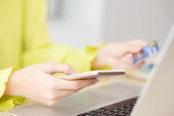 Closeup young asian business woman using smart phone and holding credit card while online shopping and payment with laptop computer on desk at home, female holding debit card, communication concept.