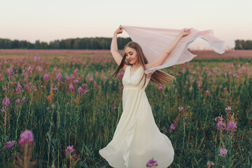 a happy girl with a white scarf walks through a flower meadow. Love and spring blooming