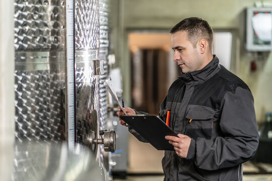 Side view of adult man winemaker at winery checking quality while standing between the silos controlling alcohol drink fermentation process - real people traditional and industry wine making concept - Powered by Adobe