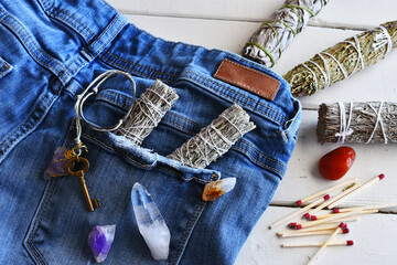 An image of sage smudge sticks and healing crystals in the pocket of a pair of jeans. 