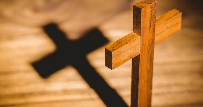 Wooden christian cross casting shadow over wooden surface
