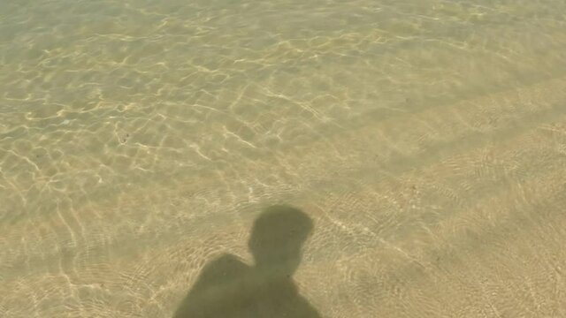 Shadow Of Person Walking along a golden sand tropical beach.