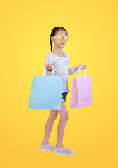 Pretty Asian little child girl wearing sunglasses holding shopping bags on yellow isolated background with clipping path. Full length