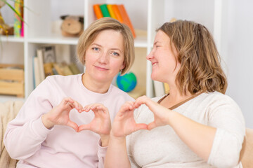 Two happy young women showing heart sign. LGBT concept