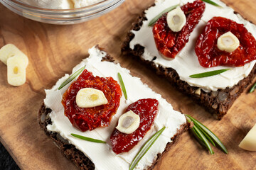 Homemade multigrain bread sandwiches with cream cheese and sun-dried tomatoes on a wooden platter, close-up. Healthy eating concept